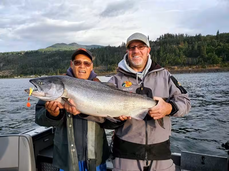 Two men proudly display a large fall chinook fish while standing on a boat