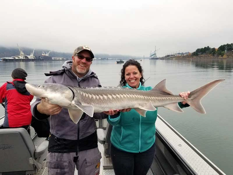 Two people on a boat holding a large sturgeon fish while winter fishing in Portland Oregon.