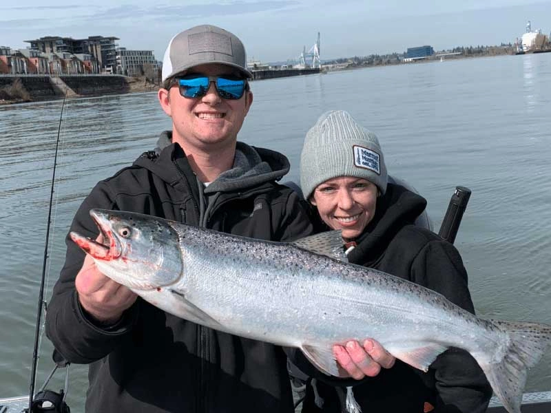 Two people on a boat holding a large fish during a spring salmon fishing in Oregon A man and woman on a boat while on a spring salmon Fishing in Oregon