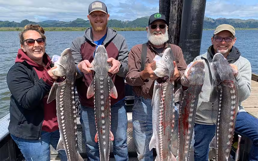 Four people holding up fish on a boat, enjoying a successful day with Columbia River sturgeon fishing guides