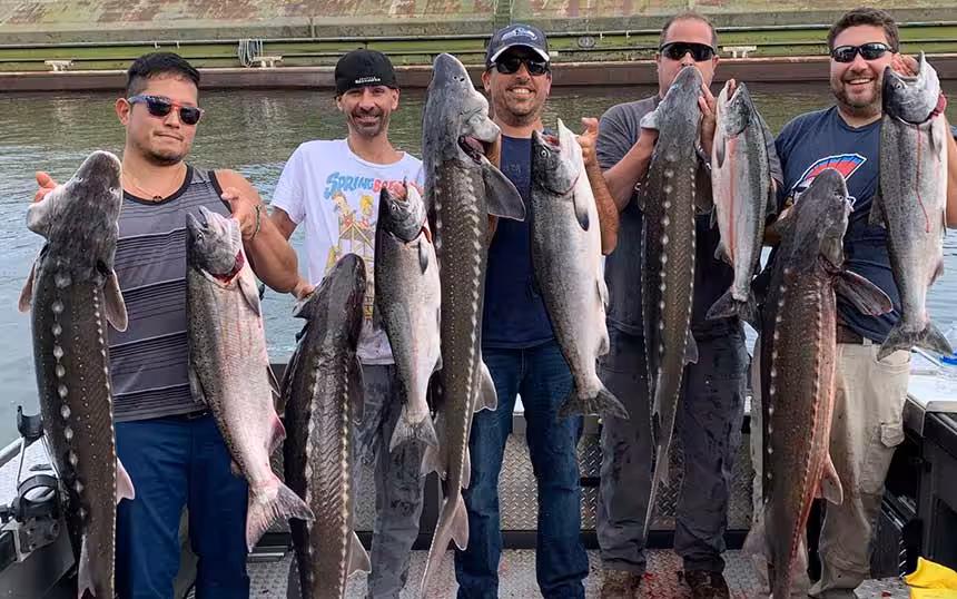 A group of men proudly displaying their catch of fish on a boat during a Columbia River sturgeon fishing trip