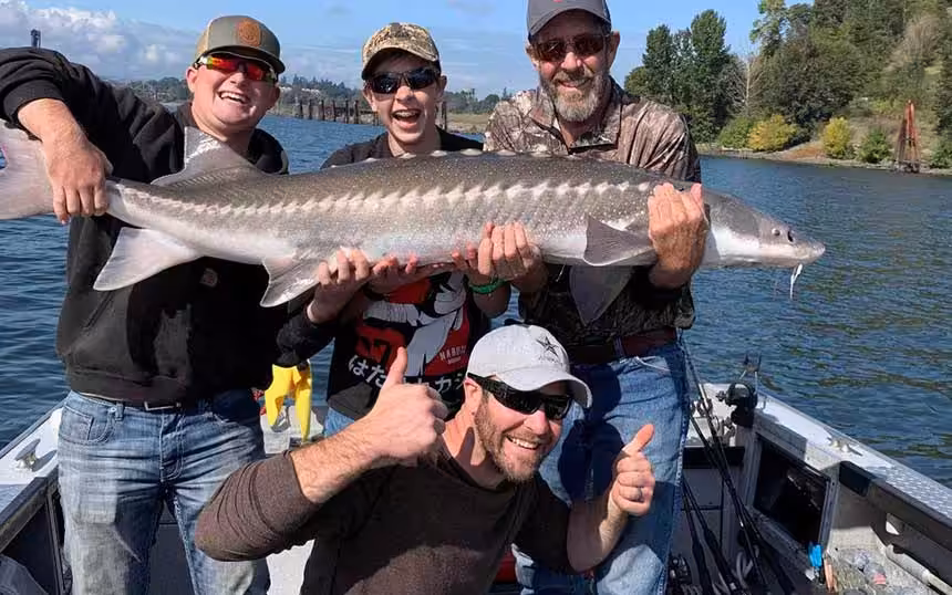 Three men pose with a massive fish they caught with the help of Columbia River sturgeon fishing guides