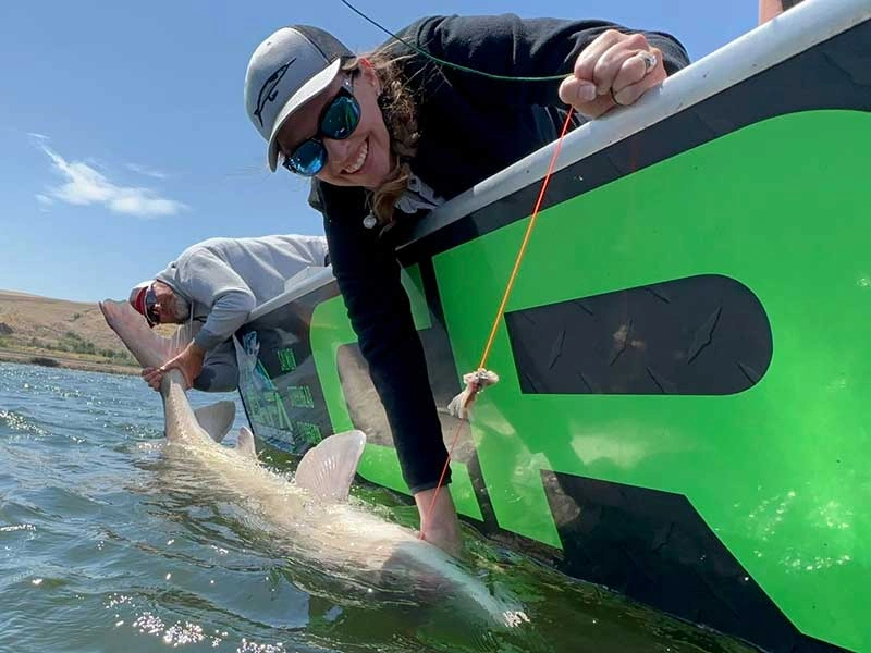 A angler smiling while holding a massive white sturgeon next to a boat during an Oregon sturgeon fishing trip.