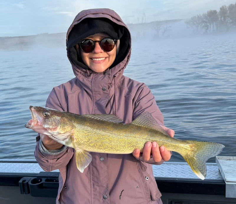 Woman on a boat holding a freshly caught fish, representing winter fishing in Portland Oregon.
