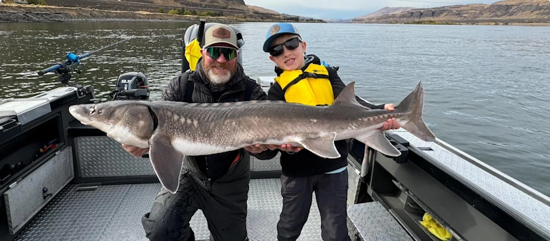 Two people on a boat holding a large sturgeon during sturgeon fishing in Columbia River