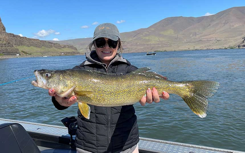 A woman joins Walleye Fishing Guide Columbia River, holds a large fish on a boat