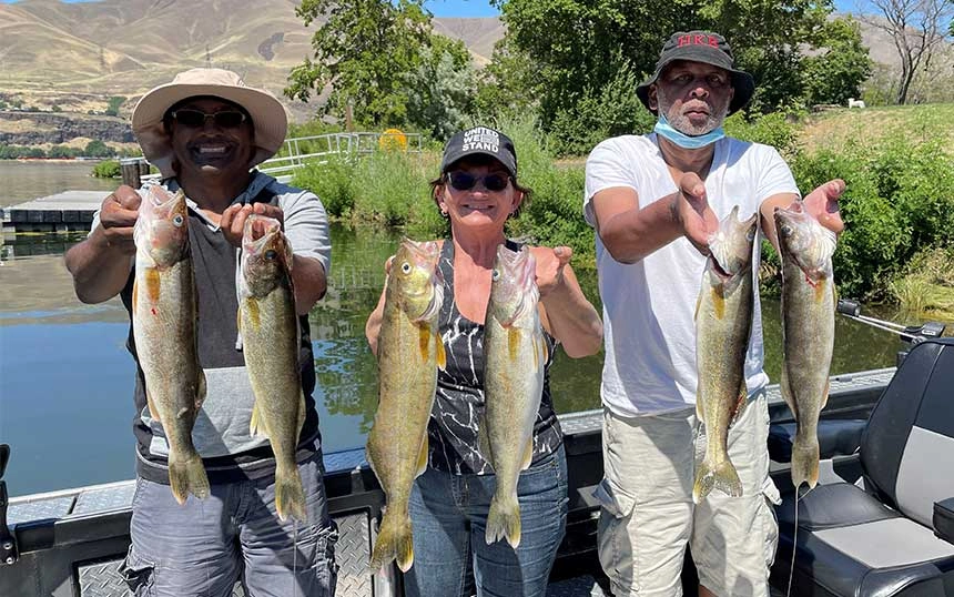 Three people on a boat holding up freshly caught fish while on Walleye Fishing Guide Columbia River