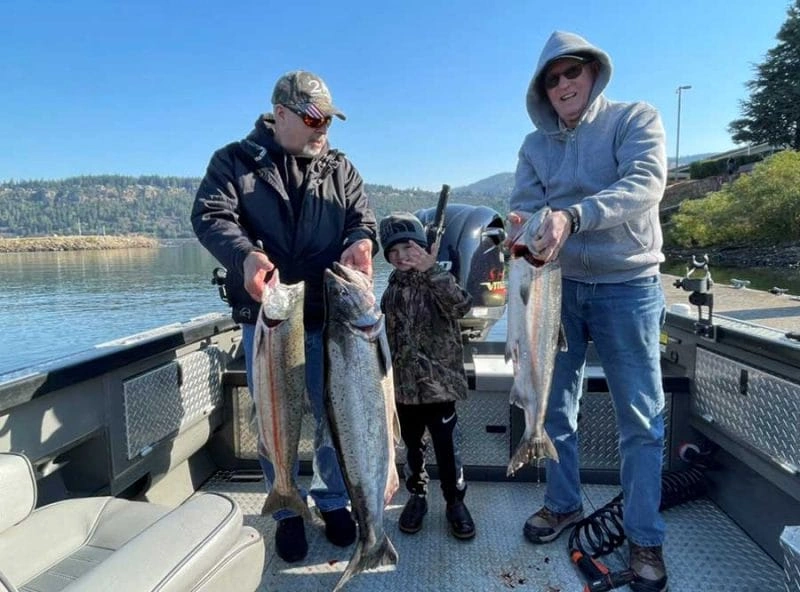 Two adults and a child holding large fish on a boat while fishing in Portland Oregon