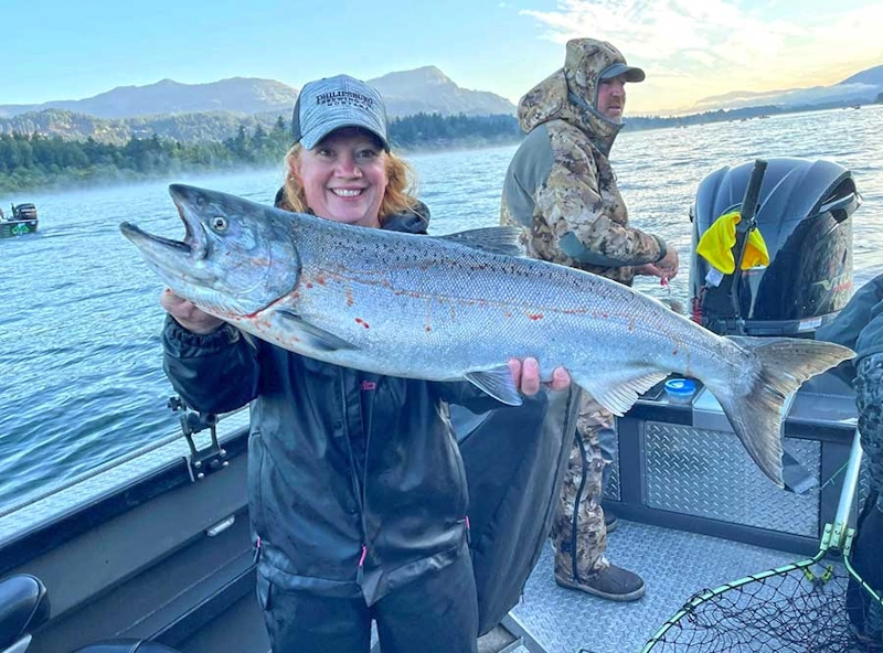 A woman poses with a freshly caught salmon on a boat, showcasing the beauty of fishing in Rufus Oregon.