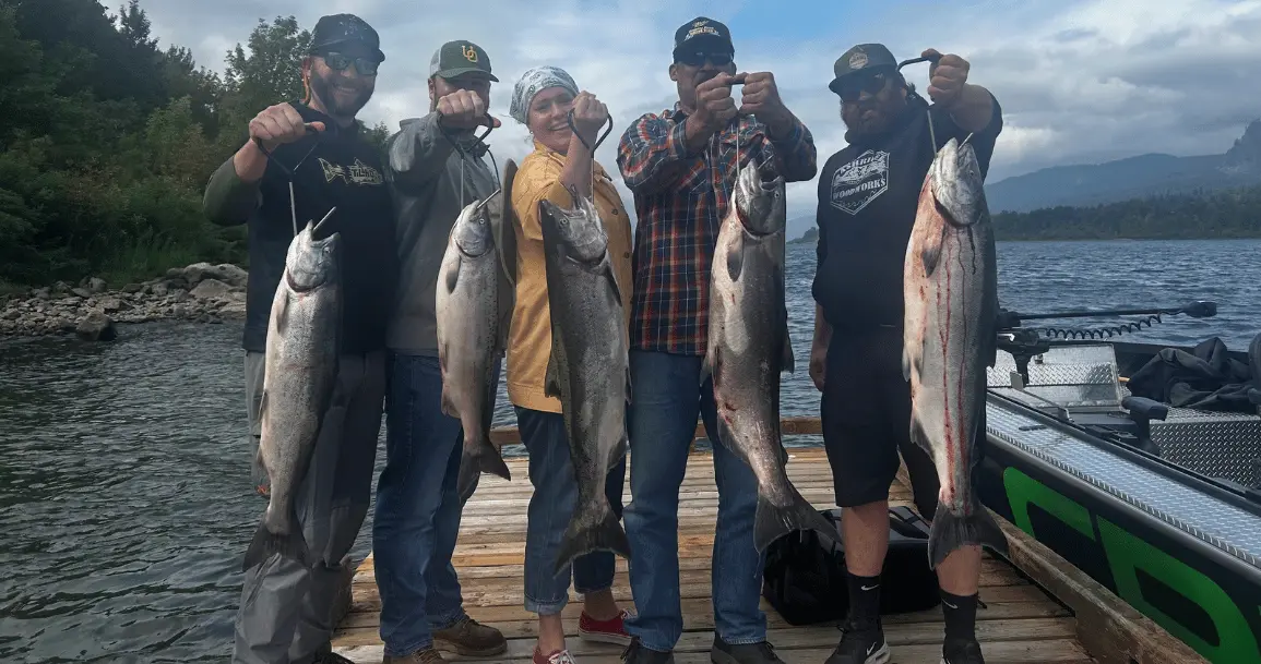 Five people holding large fish on a dock after a successful salmon fishing in Oregon.