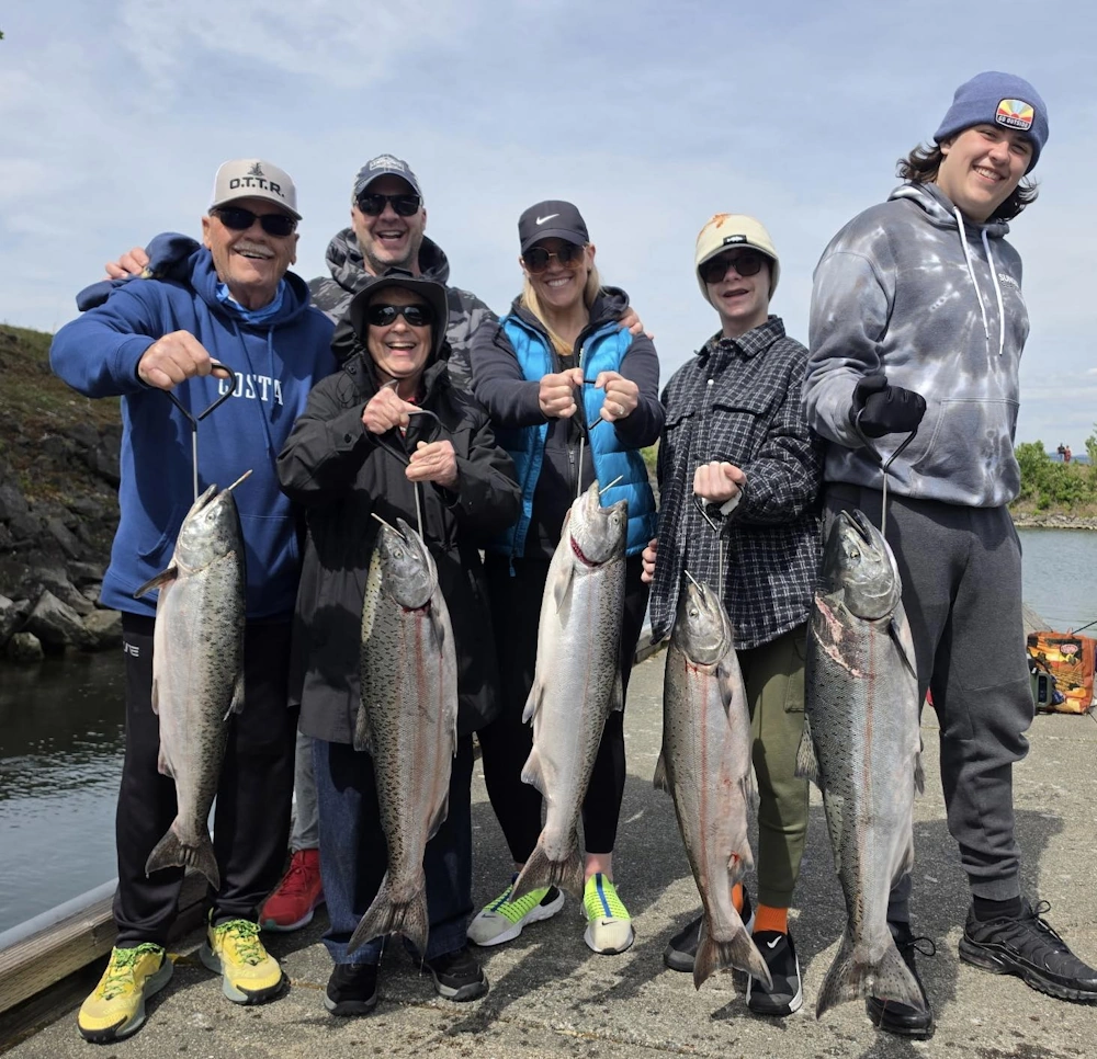 A group of six people standing on a paved pier holding five Columbia River Spring Chinook.