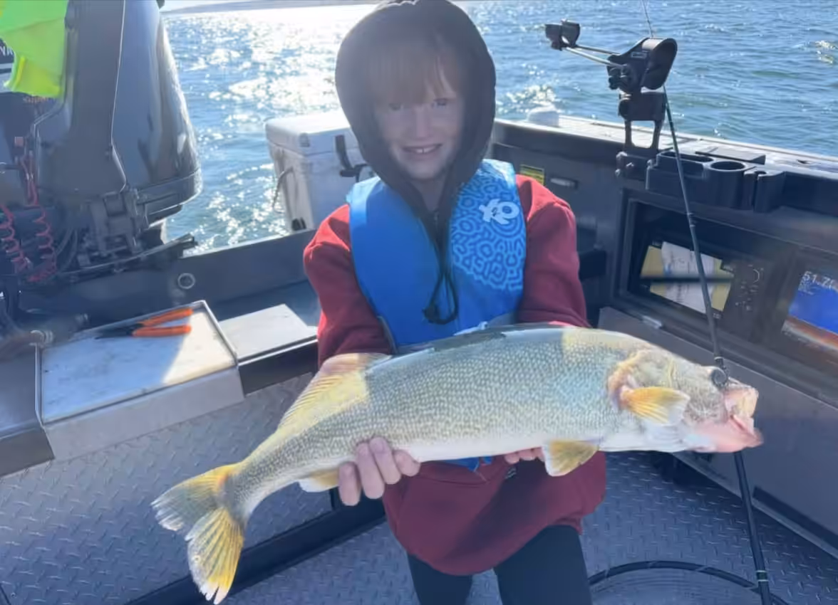 A child in a life jacket holding a large fish on a boat, highlighting the question, does a child need a fishing license for family trips.
