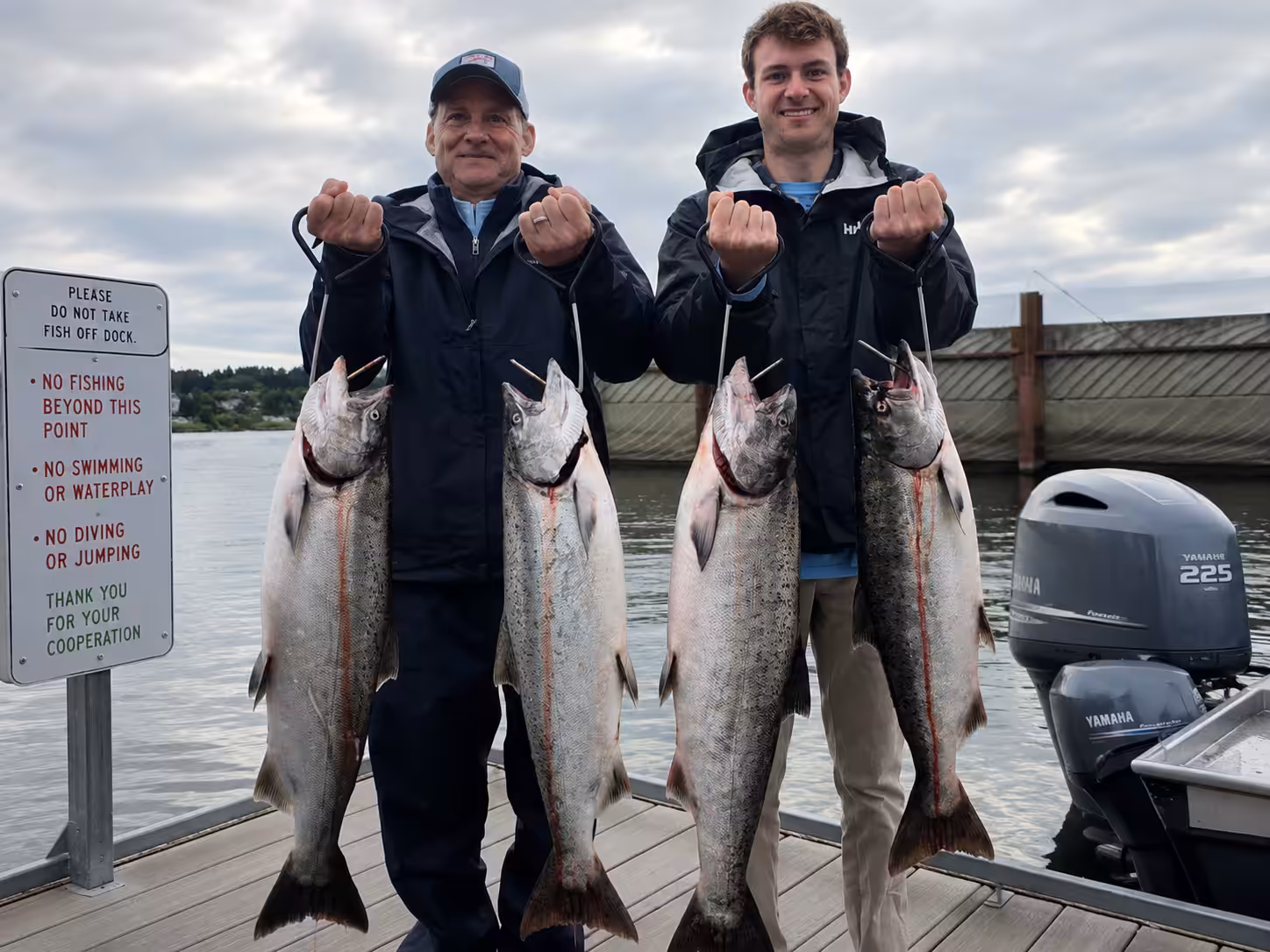 Two anglers holding up a limit of four massive salmon, showcasing the rewarding results of an active, open fishing season on the river.