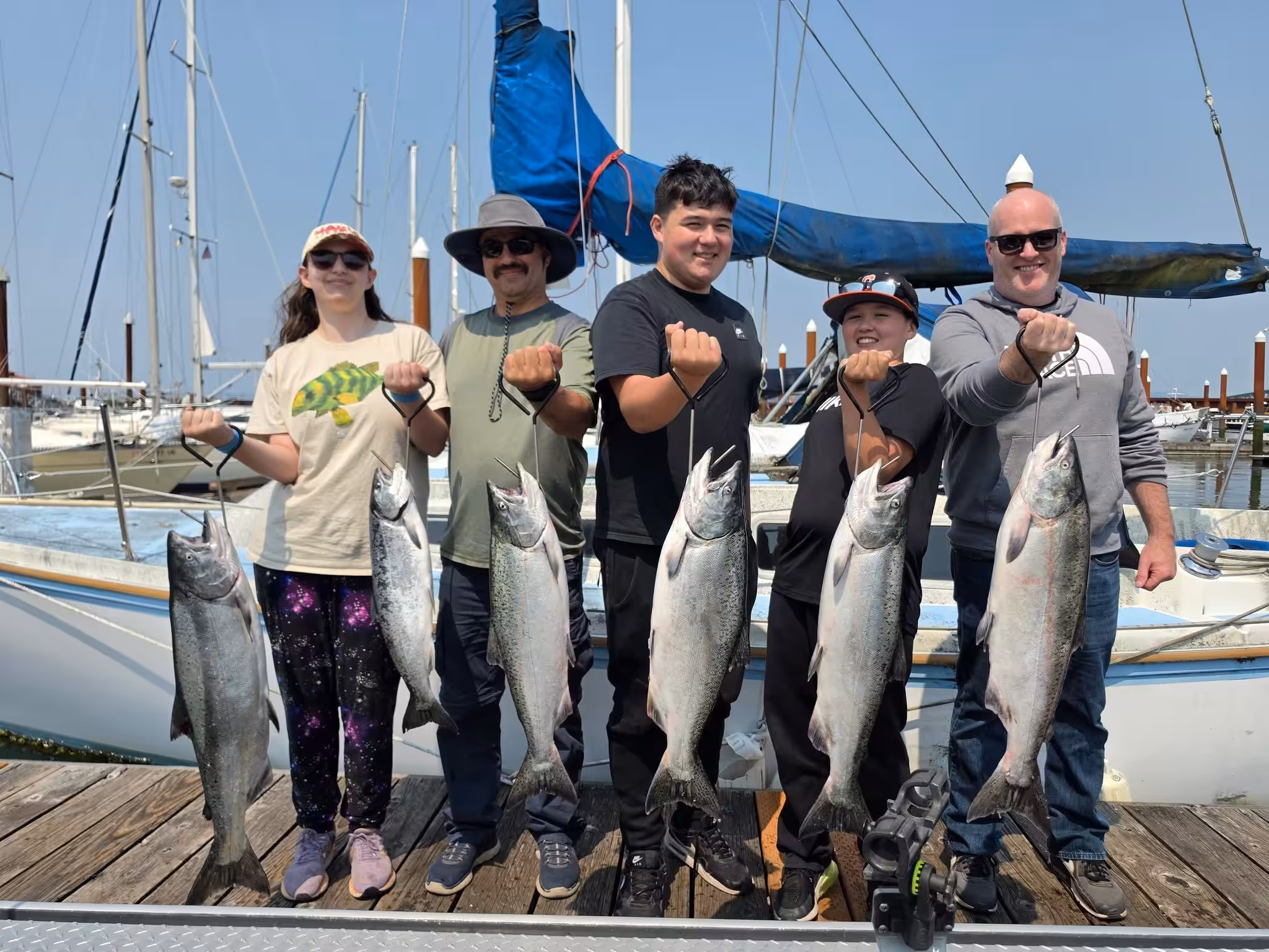 Five happy anglers standing on a dock holding large caught salmon, illustrating why people ask "is buoy 10 open for salmon fishing" to catch Chinook and Coho salmon.